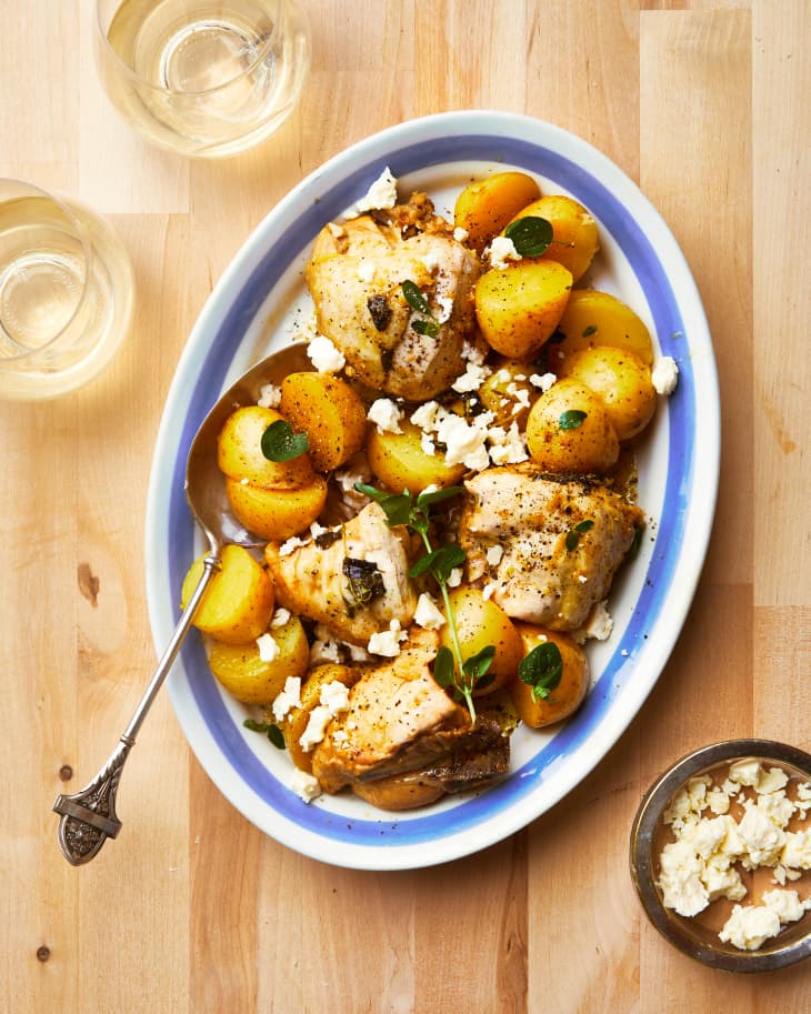Greek lemon chicken with roasted potatoes, topped with feta and fresh oregano on plate with vintage spoon on side.