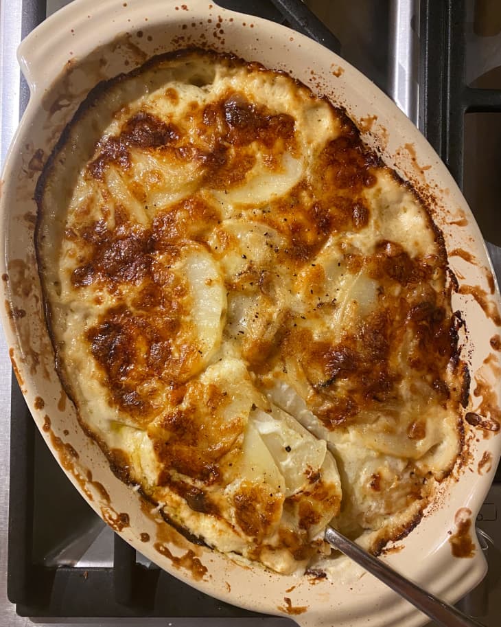 Baked potato gratin with golden brown cheese crust in an oval dish on a stovetop.