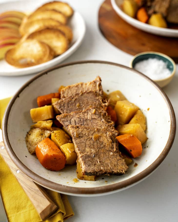 Sliced pot roast on plate surrounded by carrots and potatoes