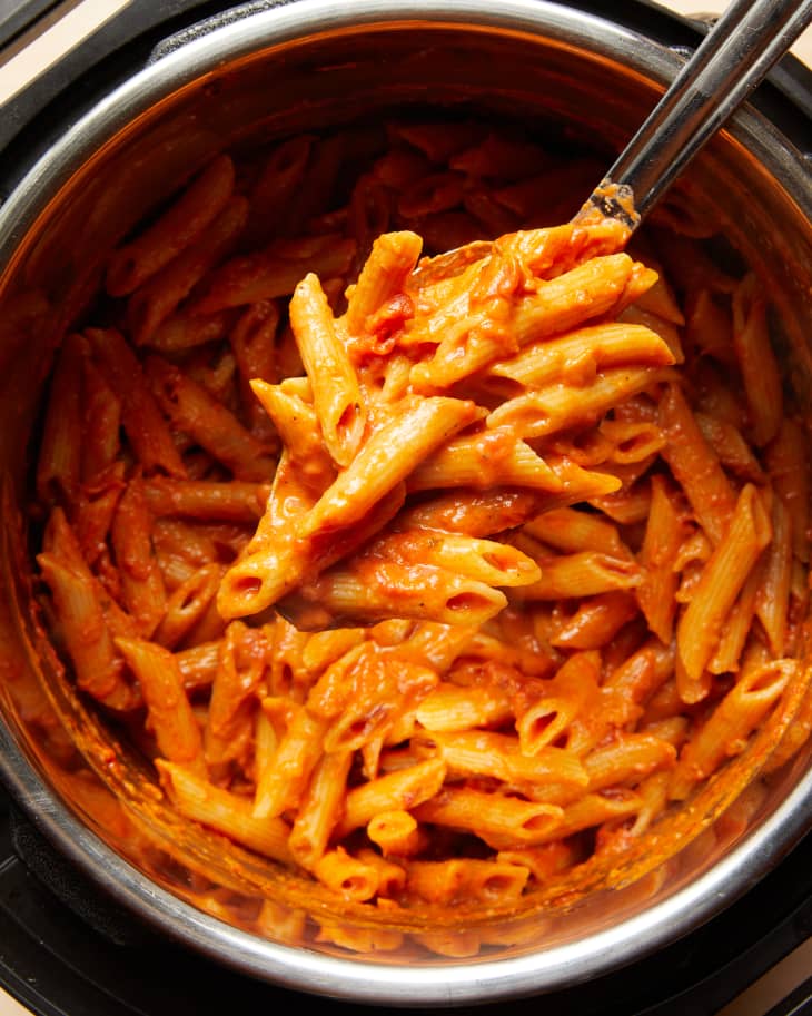 someone is pulling out a spoonful of penne pasta in an instant pot