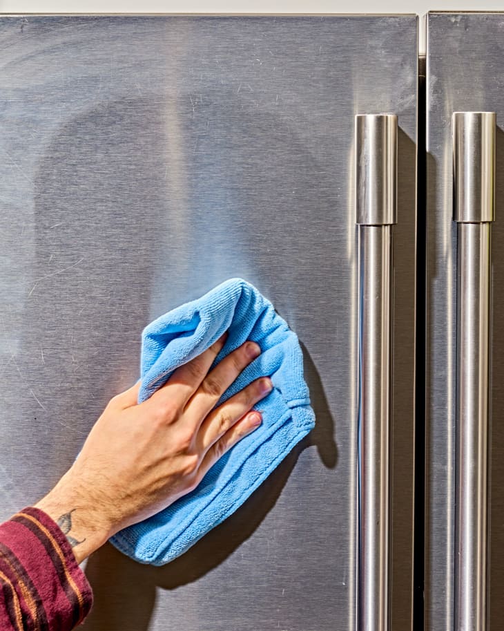 a hand wiping down a stainless steel refrigerator