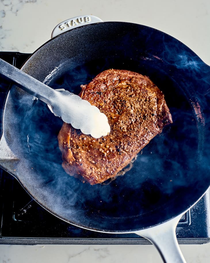 a steak being seared in a skillet