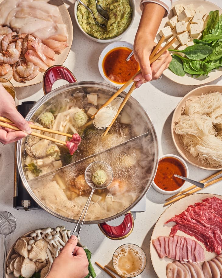 hot pot on table with things to cook in it nearby on plates