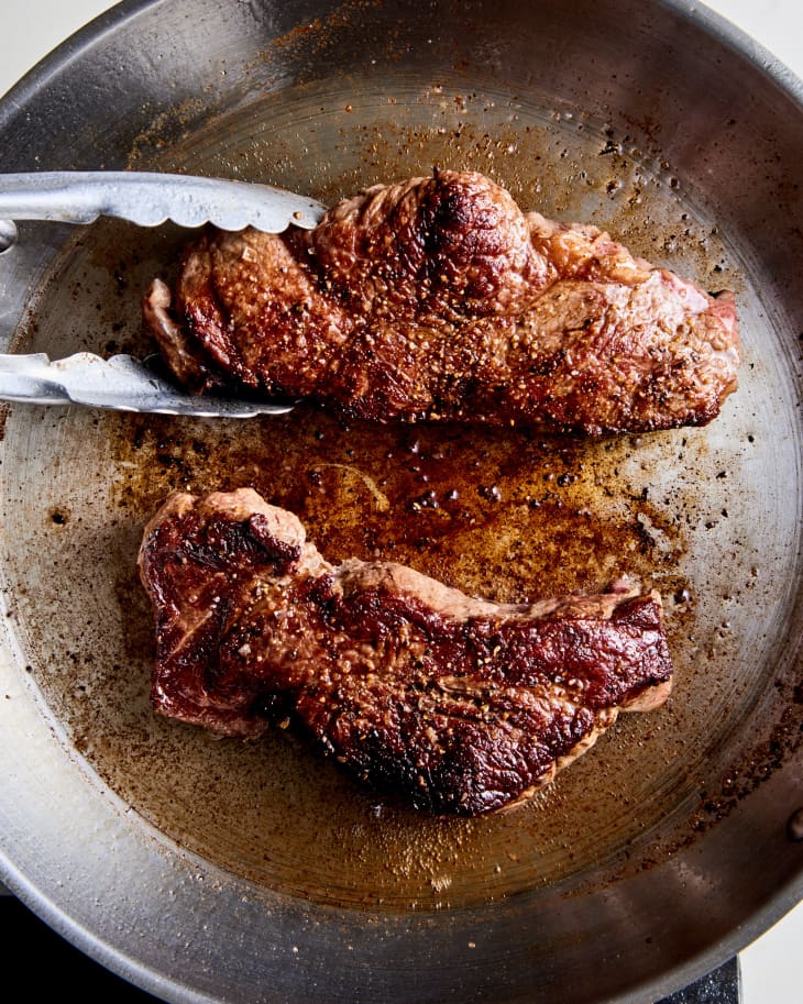 NY strip steak searing in pan, tongs removing steak
