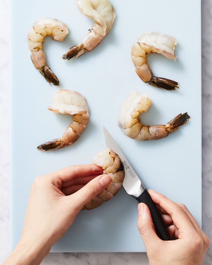 Someone slicing shrimp with butterflied shrimp on the cutting board.