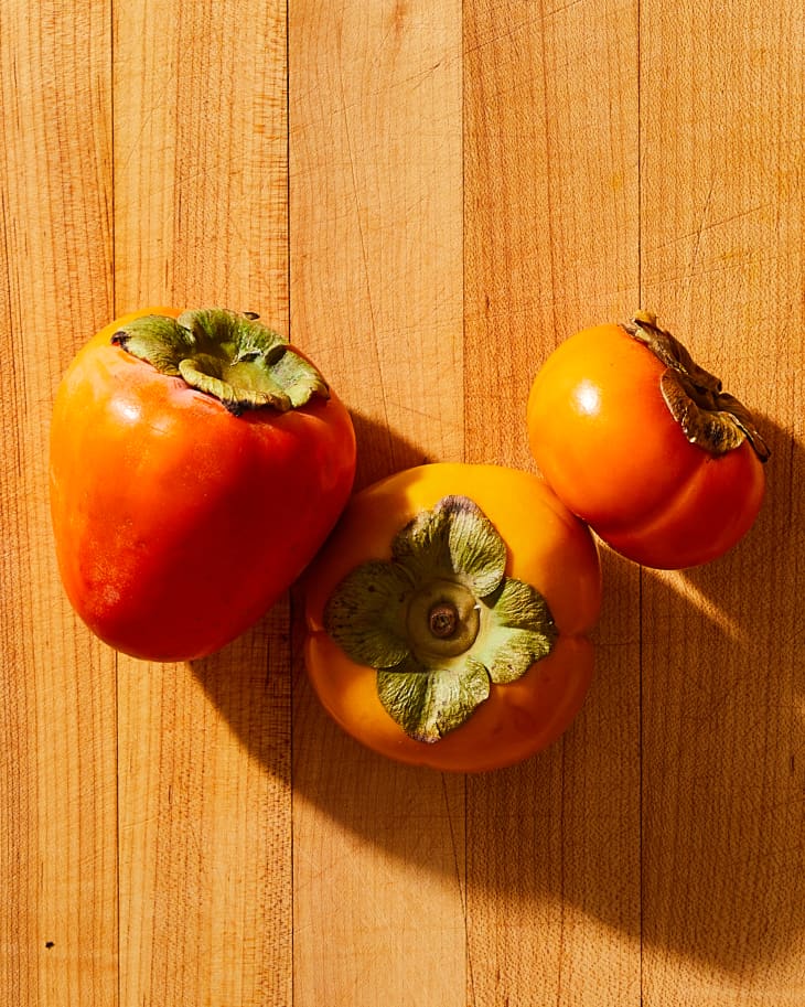 three persimmons on a cutting board