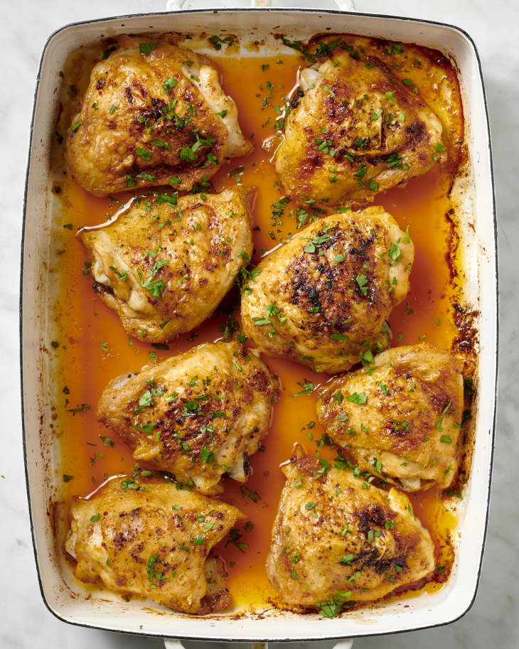 Overhead view of cooked chicken thighs in a white pan topped with herbs.