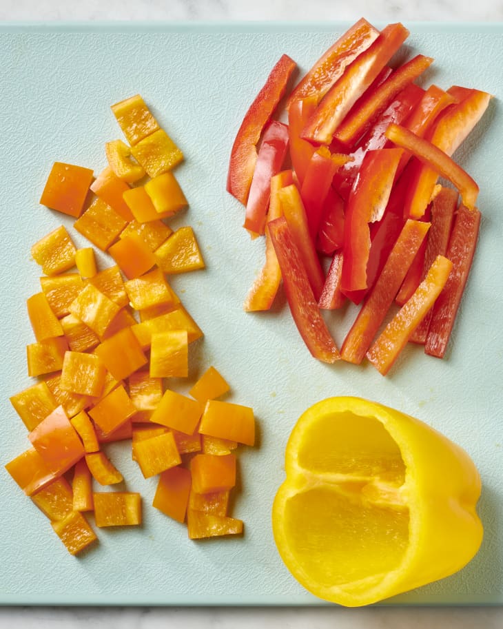 Overhead view of on cored yellow bell pepper, one cubed orange bell pepper and one red bell pepper cut into strips.