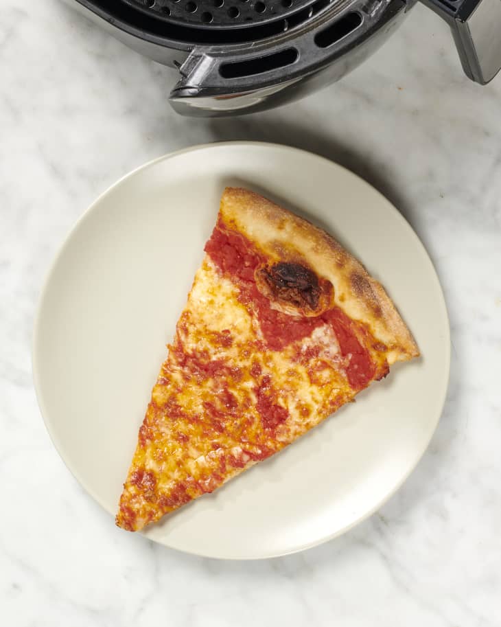 Overhead view of a slice of pizza on a white plate, with an airfryer peeking into the shot on the top.