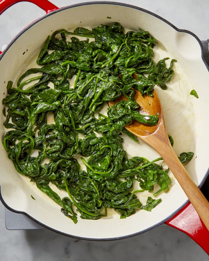 Overhead shot of spinach being cooked down in a pan, and stirred by a wooden spoon.