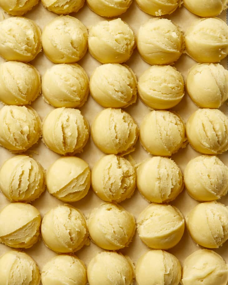 Overhead shot of scoops of sugar cookie dough on brown parchment paper in a metal sheet tray.