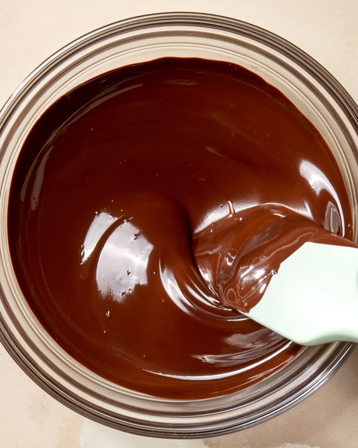 Overhead shot of melted chocolate in a glass bowl with a blue spatula stirring it.