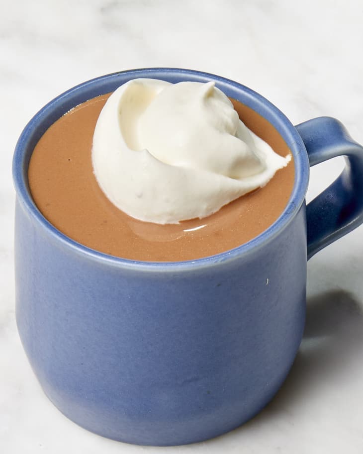 Angled shot of Jacques Torres' hot chocolate recipe in a dark blue mug, topped with whipped cream.