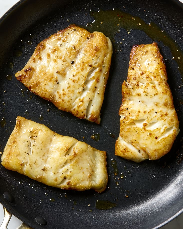 overhead shot of three pieces of white fish in a black frying pan.