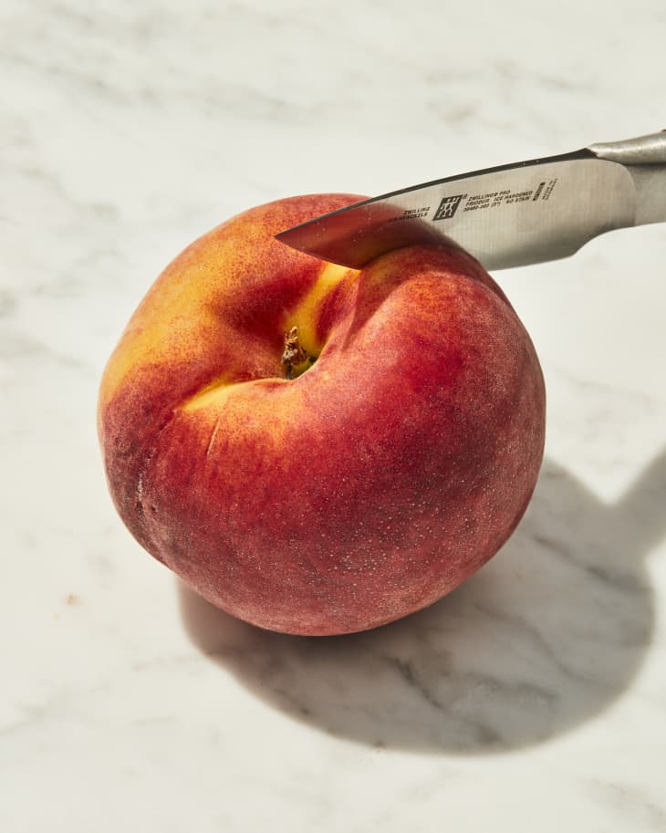 Knife cutting through peach