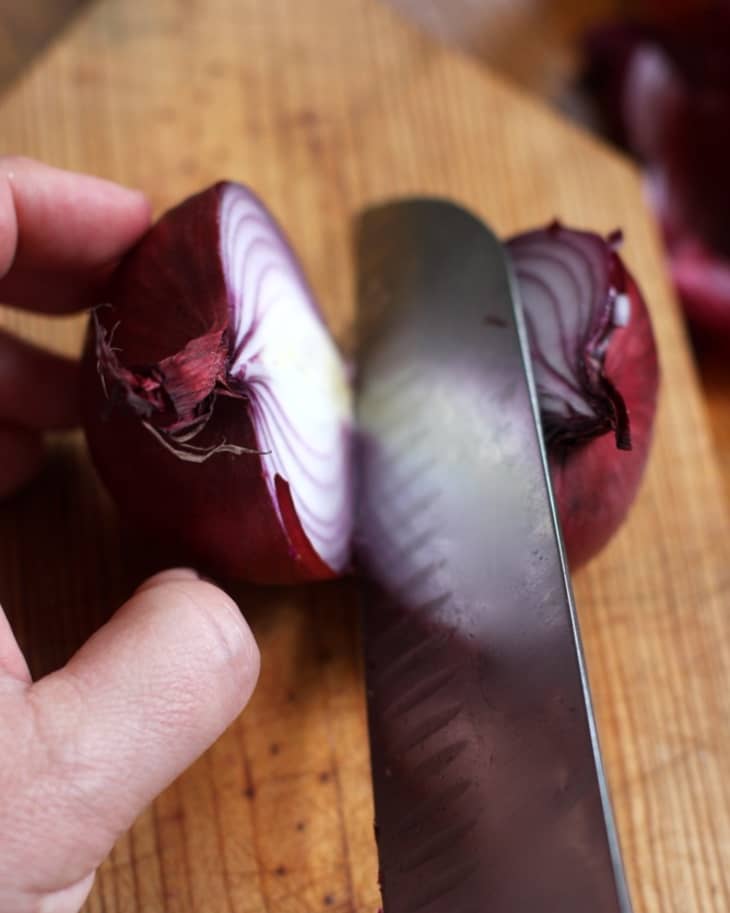 Someone slices a red onion into half