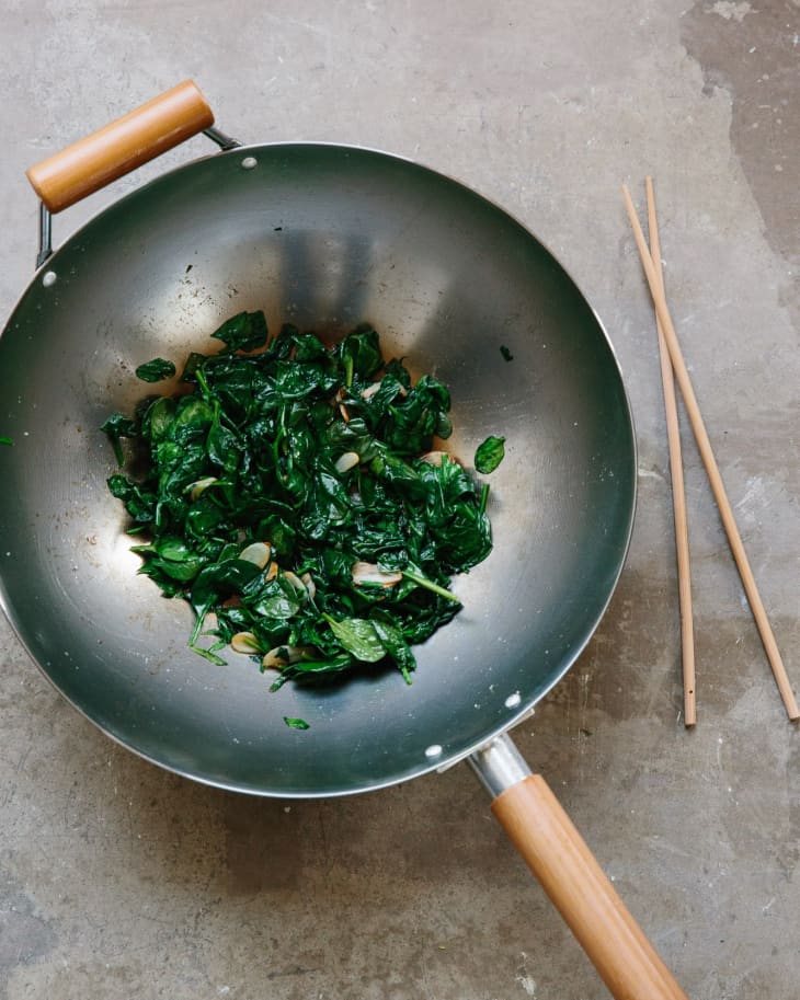 Stir-fry spinach with garlic in a wok, with chopsticks on the side