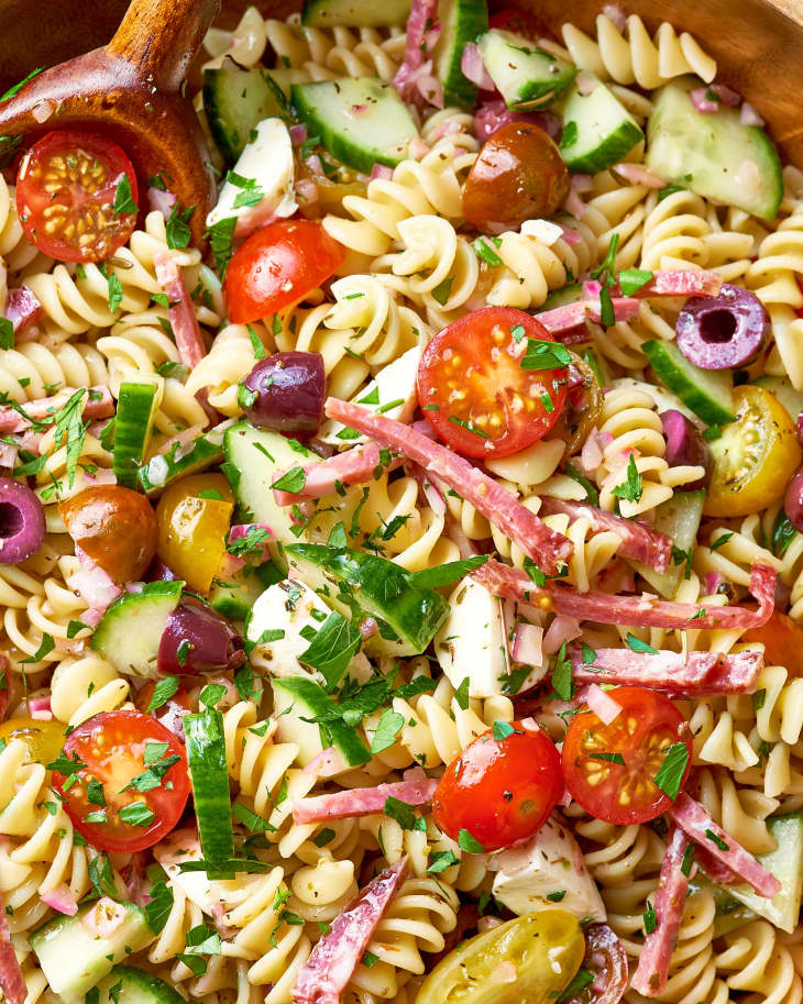 Close-up of pasta salad with halved cherry tomatoes, sliced kalamata olives, chopped English cucumber, cucumbers, and salami