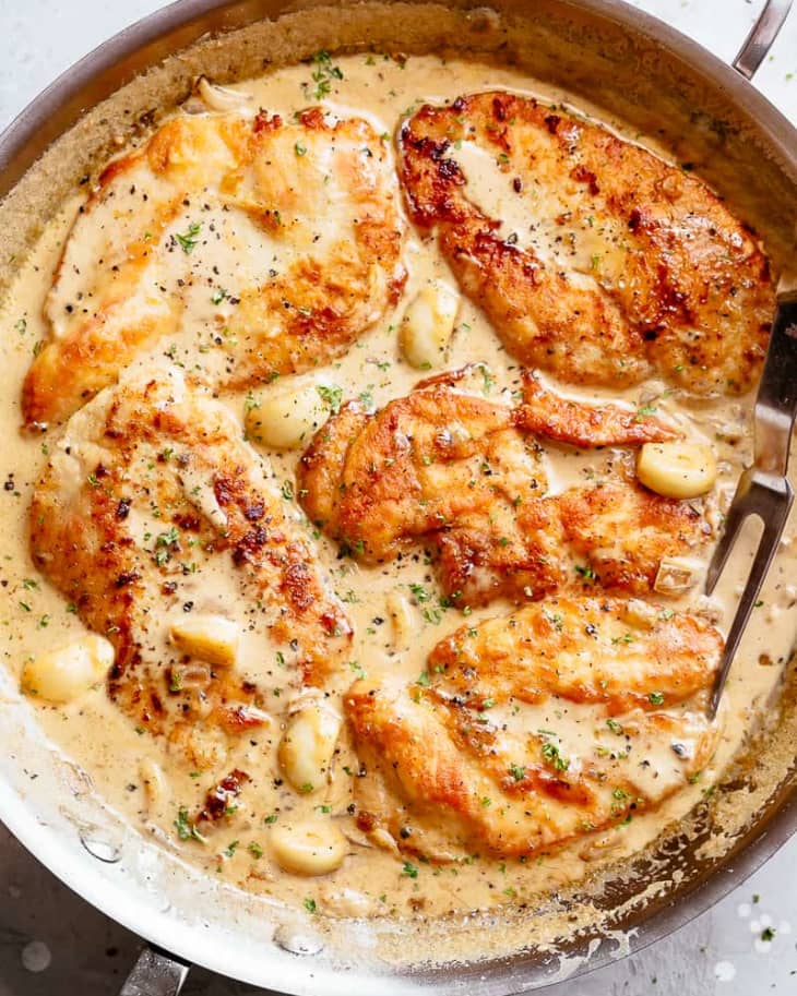 Creamy garlic chicken breasts in a skillet with herbs and sauce.