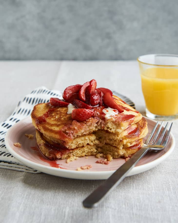 A stack of cornbread pancakes on a plate and topped with strawberries and syrup with a wedge cut out