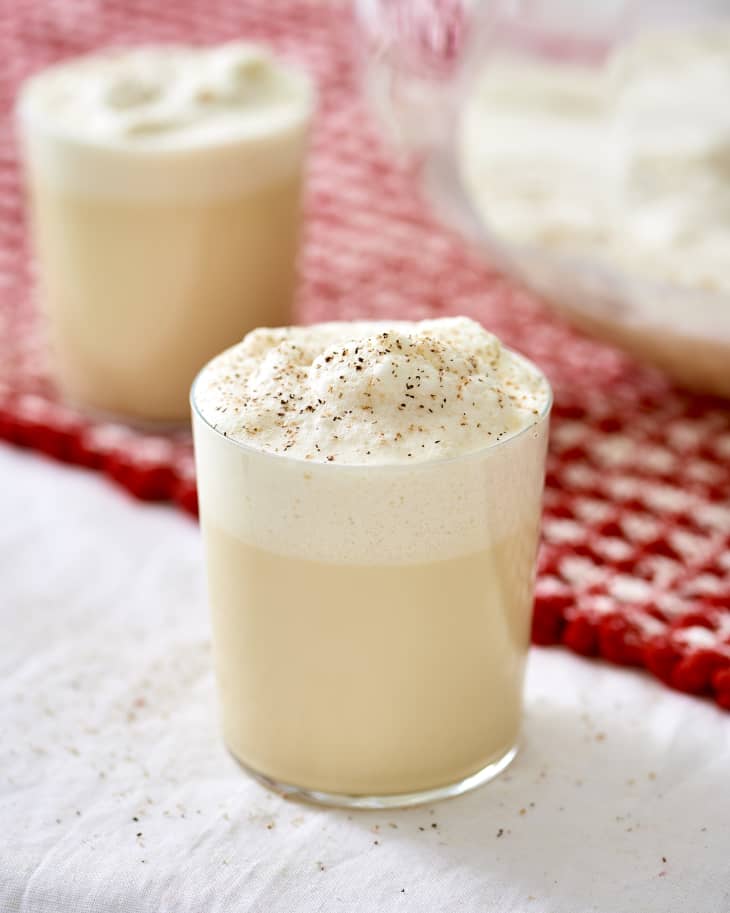 Eggnog on a white tablecloth in a glass with nutmeg sprinkled on top.