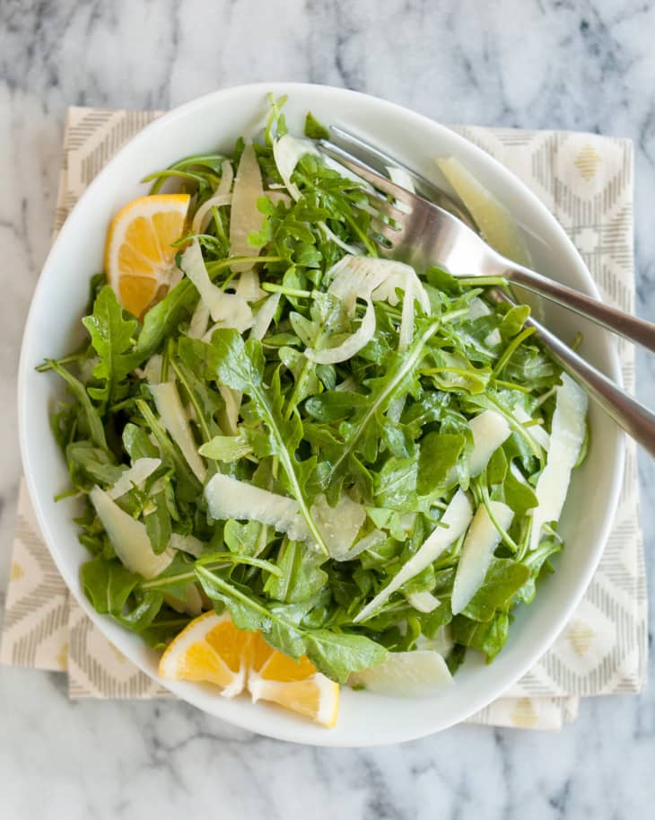 Arugula and fennel salad with Pecorino cheese and two slices of orange in a bowl with two forks on it