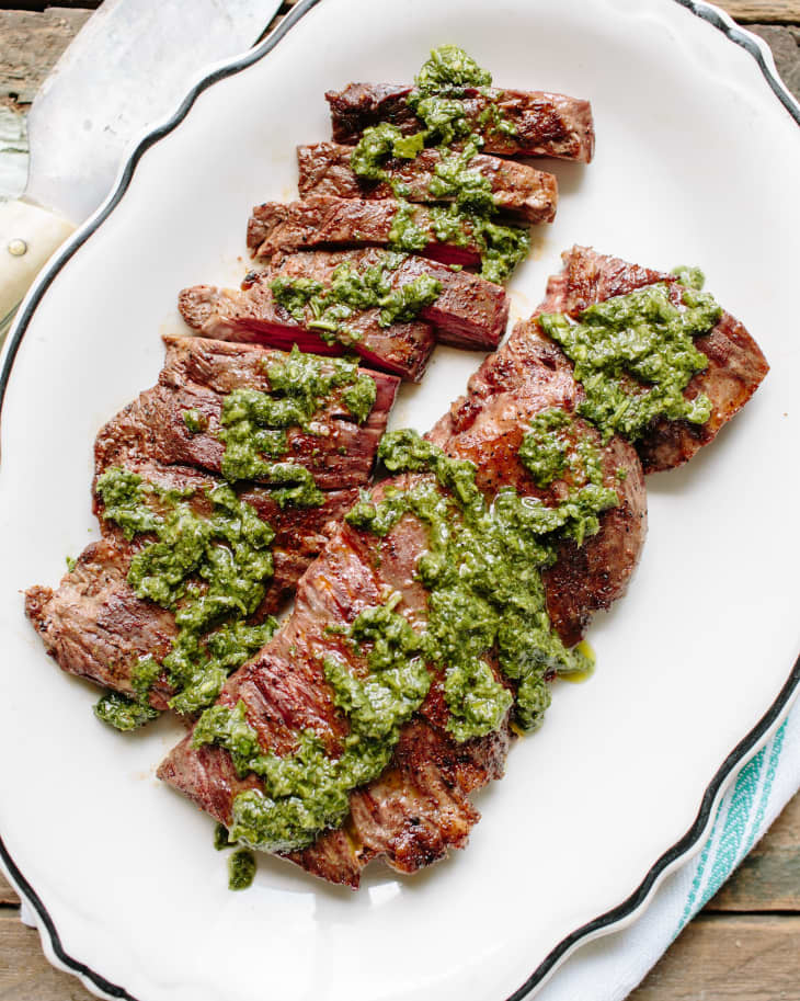 Two slabs of beef, topped with some pesto sauce, on a serving platter