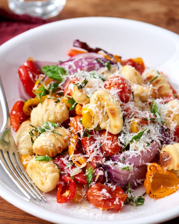 Gnocchi with roasted cherry tomatoes, red onions, and grated cheese on a white plate.