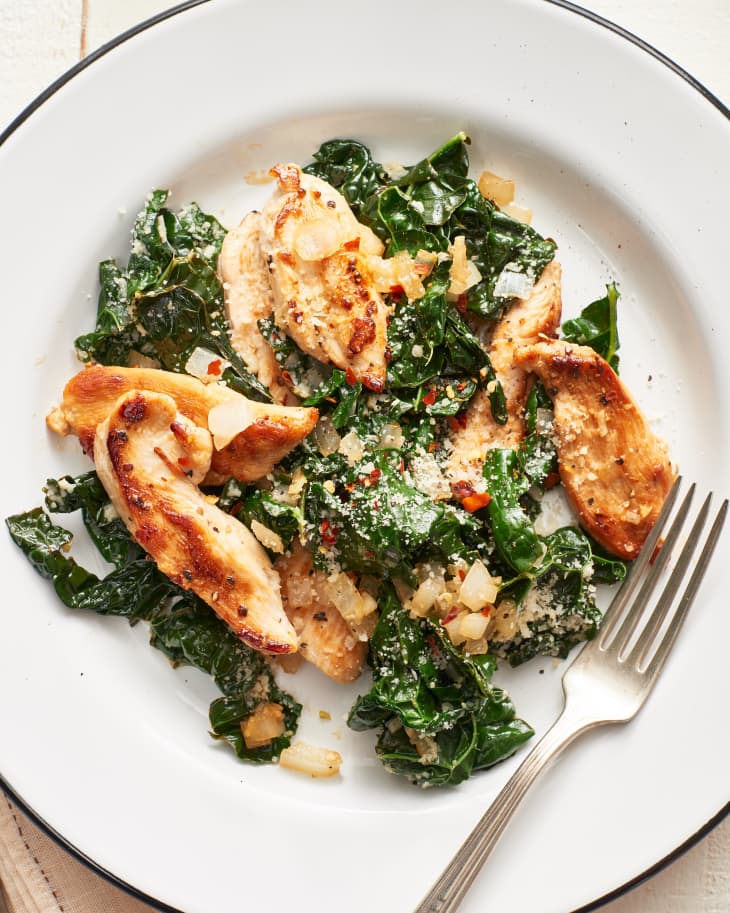 Chicken and kale sauté with Parmesan cheese on a plate with fork besides it