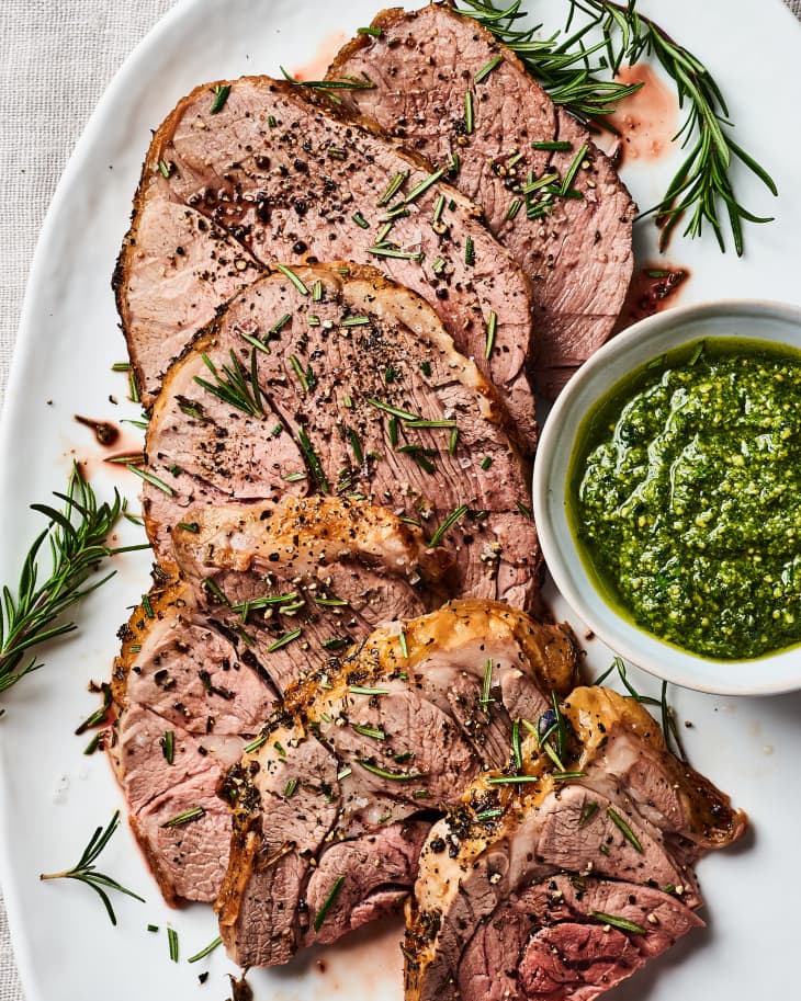 A roasted leg of lamb cut on a platter with a mint dipping sauce