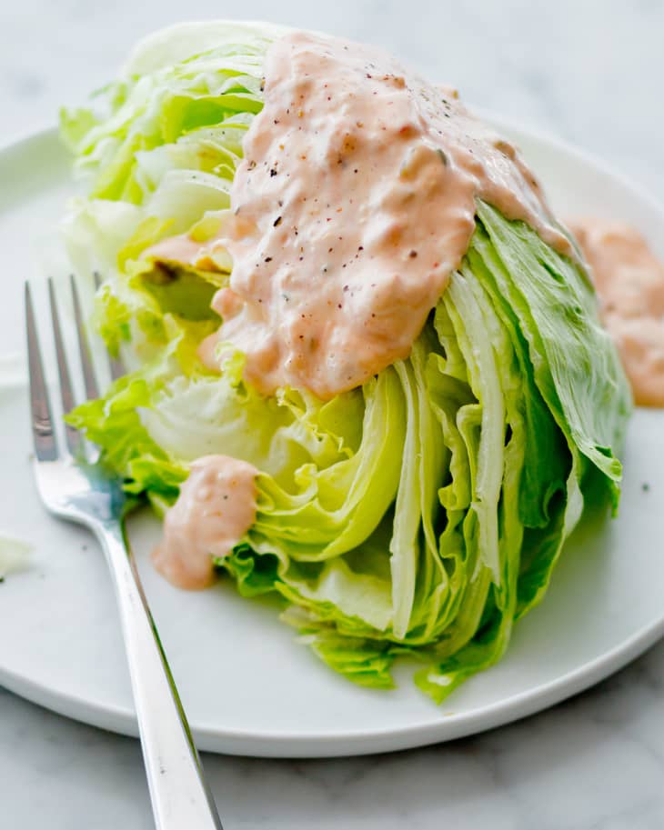 A wedge of iceberg lettuce on a plate drizzled with Thousand Island dressing