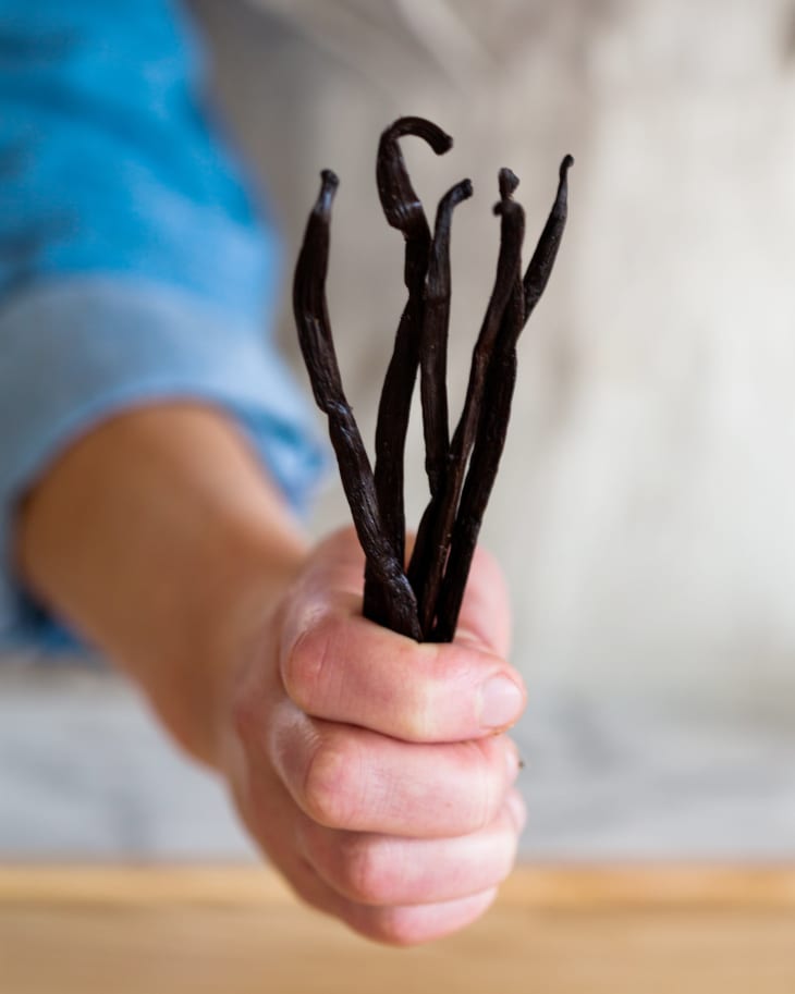 A person holds five vanilla beans in one hand
