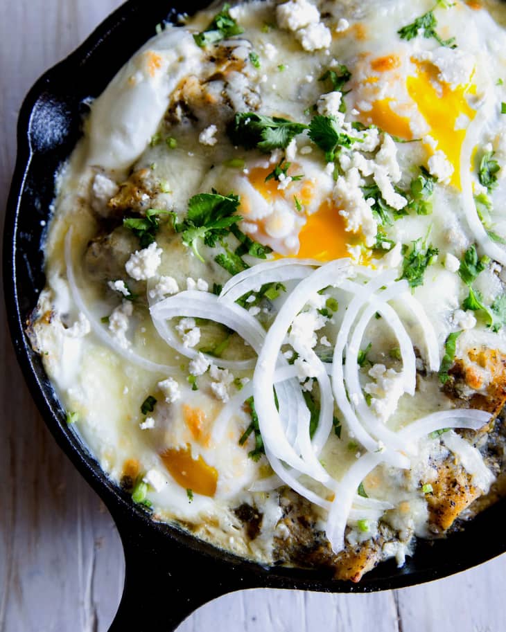 A cast iron skillet with breakfast enchiladas topped with cotija and sliced onions