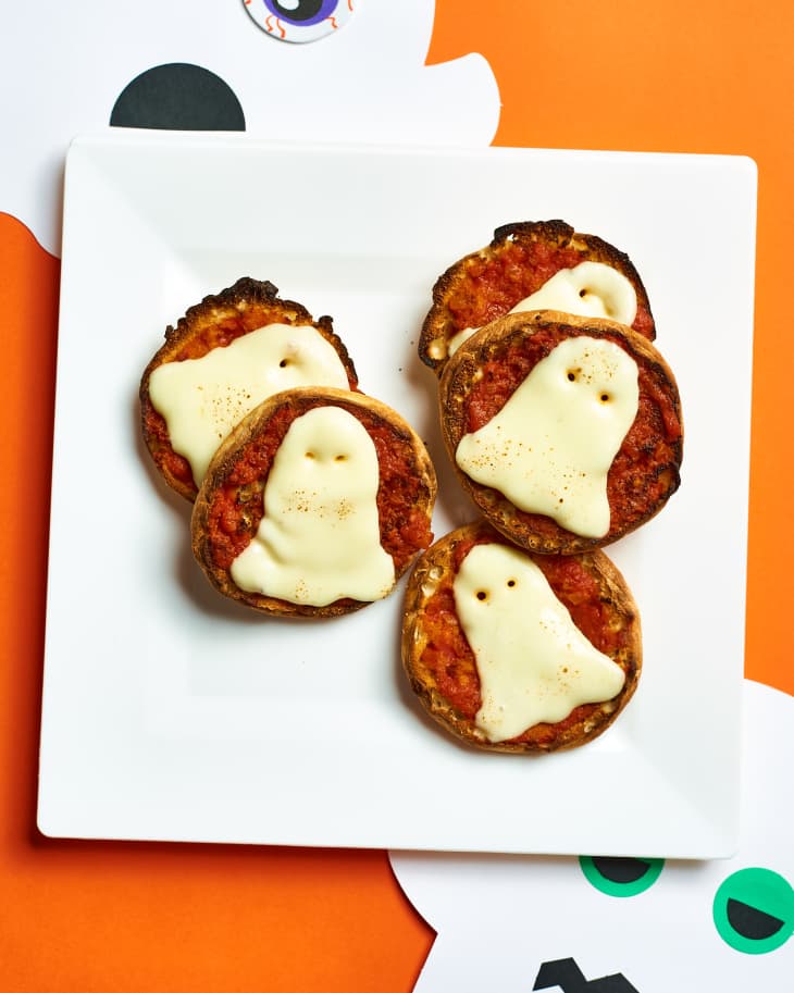 Image 3: Mini pizzas topped with ghost-shaped cheese slices on a white plate, set on an orange background.