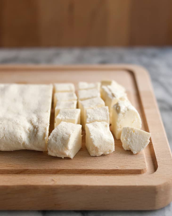 Paneer cheese cut in cubes lay on a wooden chopping board