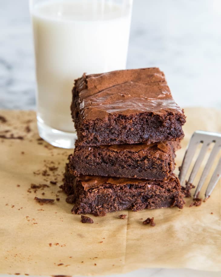 A stack of three brownies with a glass of milk in the background