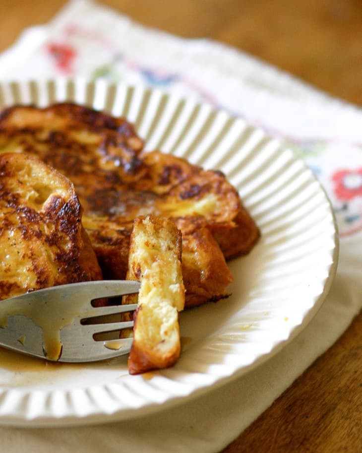 Partial view of French toast on a plate, one piece speared by a fork