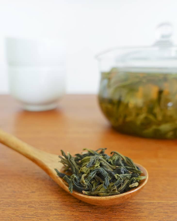 Dried oolong leaves on a wooden spatula, with oolong tea in the background