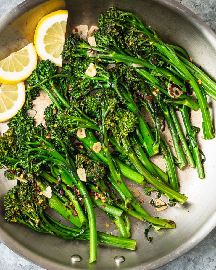 Broccolini with garlic and lemon wedges in a pan