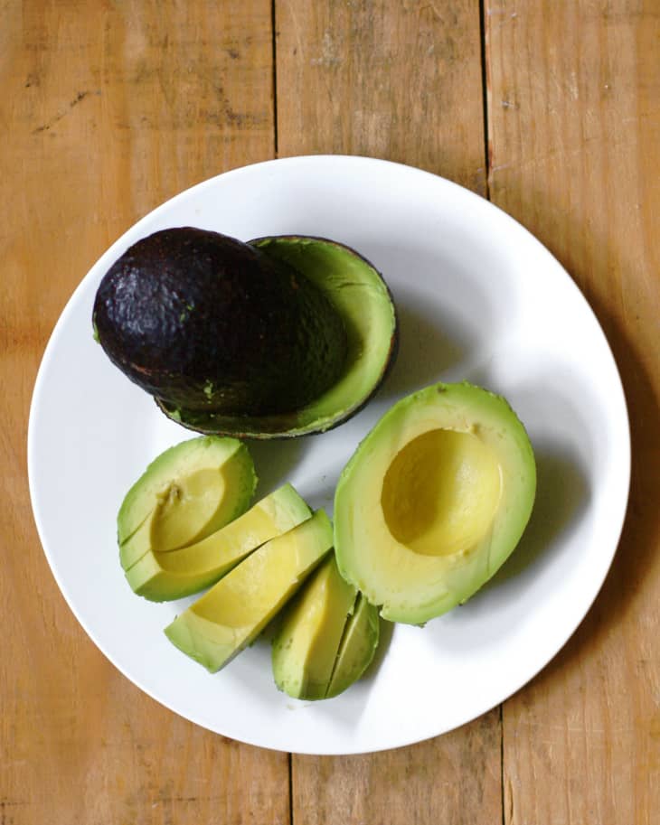 An avocado cut in half, sliced and pits removed on a white plate