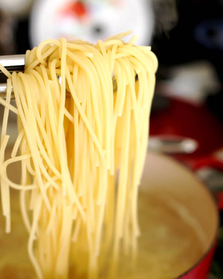 Tongs pulling cooked spaghetti noodles out of a pot of water