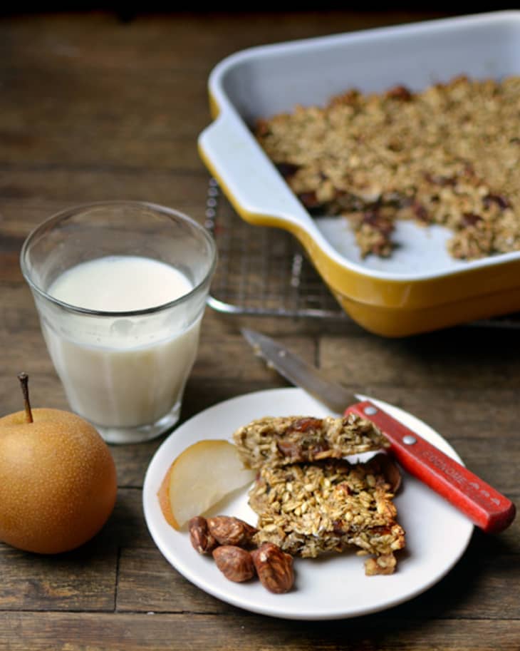 Banana oat bars, with a slice of pear and dates, on a plate, served with a glass of milk and fruit pear on the side