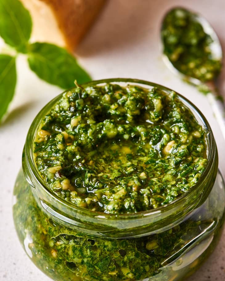 Interior view of jar of homemade pesto with spoon filled with pesto in the background