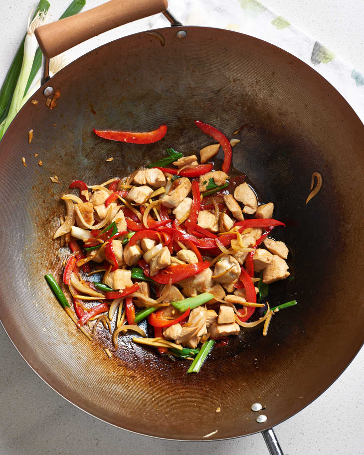 Chicken is stir-fried with ginger, scallions, onions, and bell peppers in wok