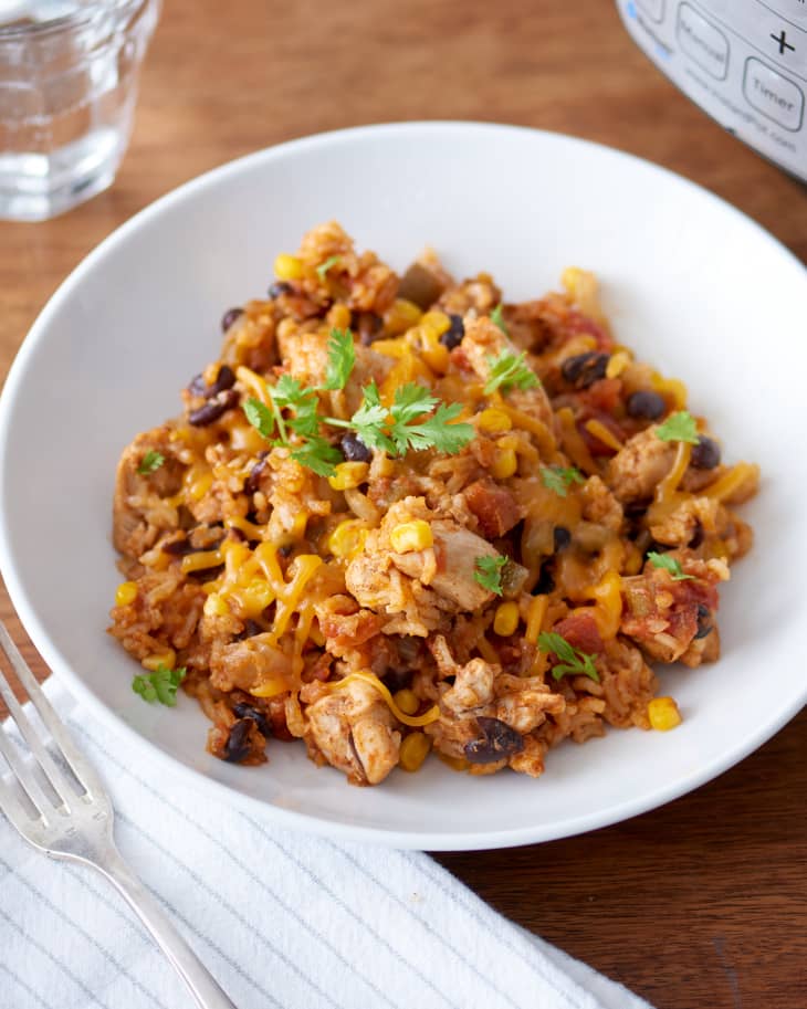 A bowl of chicken and rice with corn, black beans, and cheese, garnished with cilantro.