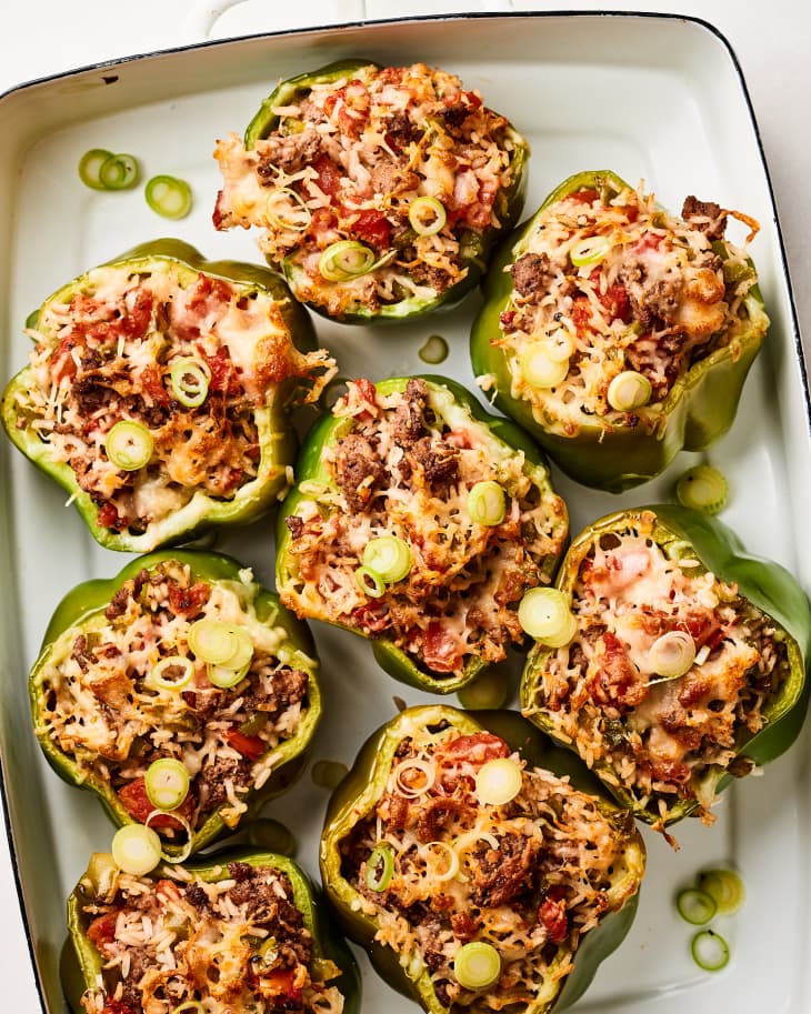 Stuffed green bell peppers with rice, ground beef, tomatoes, and melted cheese, garnished with sliced green onions.