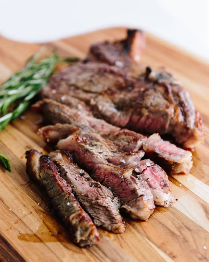 Steak sliced up on a wood cutting board with a few sprigs of fresh rosemary