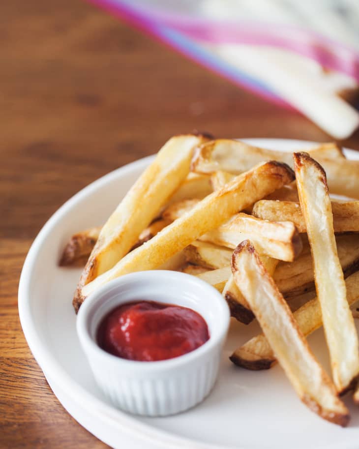 A plate of French fries with a small dish of ketchup