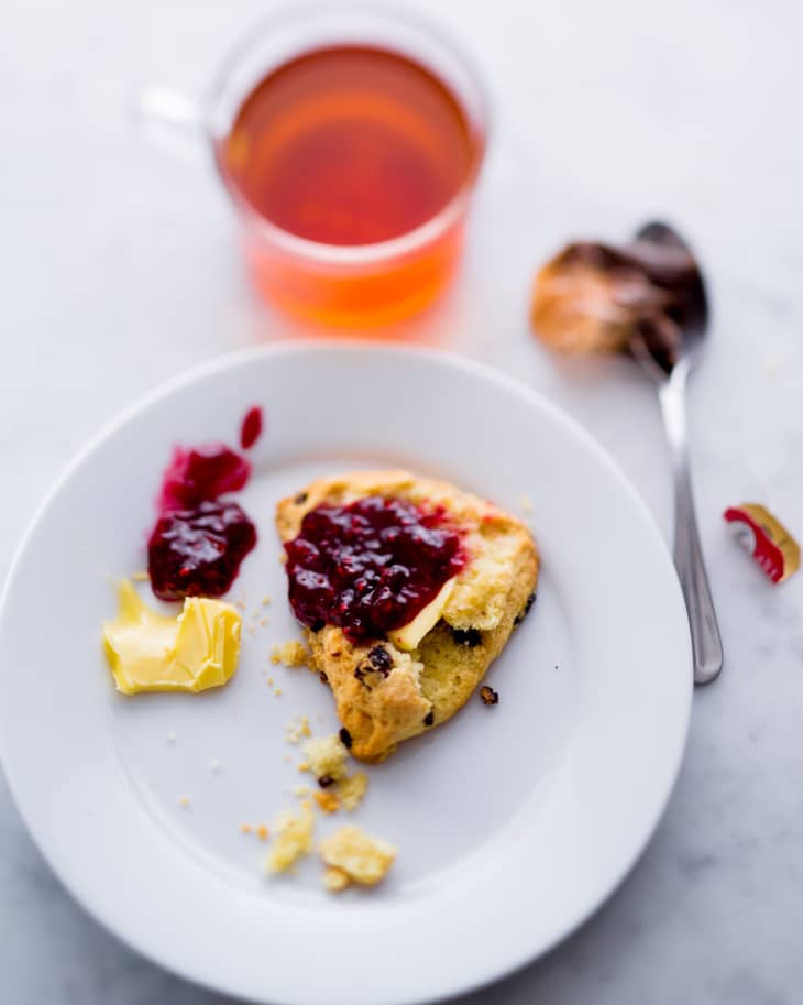 Scone with butter and jam on a plate alongside tea and a spoon