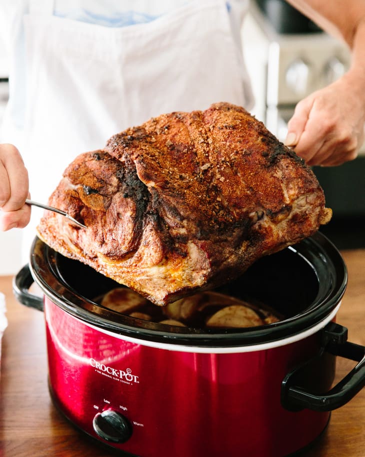 A person lifts the pull pork up from a red crockpot